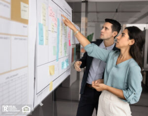 Two analysts engaged in focused discussion in front of large whiteboard filled with diverse sticky notes.