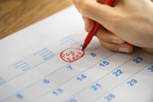 A woman's hand circles the "Pay Rent" date on her calendar.
