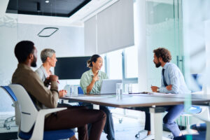 Four businesspeople sitting around a table in a modern office, engaging in a project discussion.
