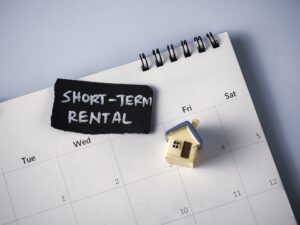 Calendar showing short-term rental dates with a house model and a sign indicating "Short Term Rental”.