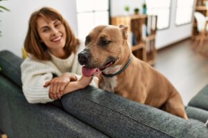 A woman smiling, sitting on the sofa in a rental home with her dog.