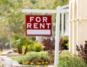 A for-rent sign is in the yard of a sunny home.