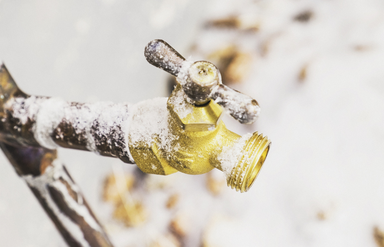 Frozen Outdoor Water Faucet and Pipes Covered in Snowflakes