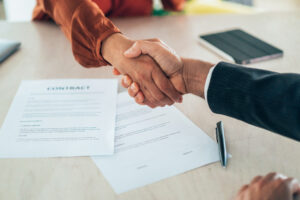 A business handshake over contracts, representing the agreement to hire a property manager.