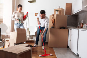 A man and woman tidying a room filled with boxes, organizing, and cleaning the space together.