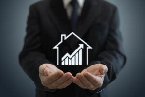 Line drawing of house containing an upward trending graph in front of businessperson holding out their hands. 