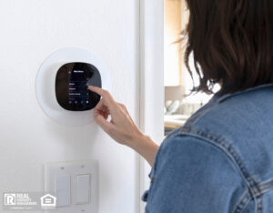 A woman programming a smart thermostat at home.
