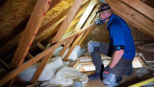 Home inspector kneels inside a finished attic of a residential property.