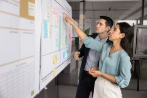Two analysts engaged in focused discussion in front of large whiteboard filled with diverse sticky notes.