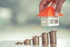 Image of a house over stacks of coins, symbolizing the upward trend in the housing market.