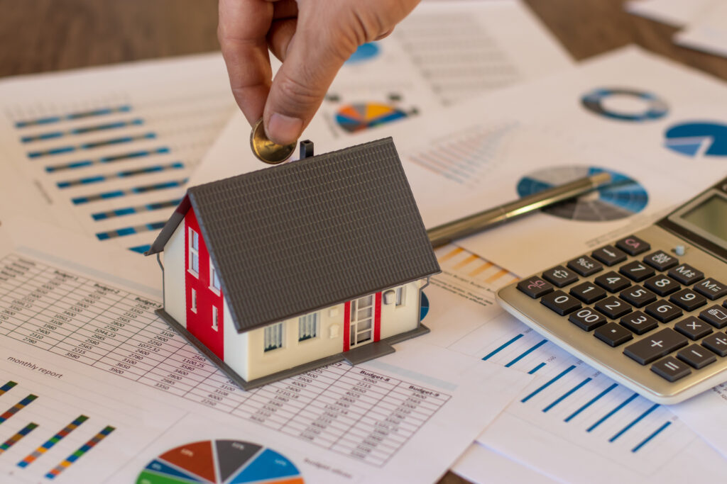 Hand placing coin on house model on table with financial documents. 