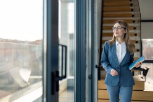 Modern female property manager, wearing suit and eyeglasses holding notebook ready for meeting.