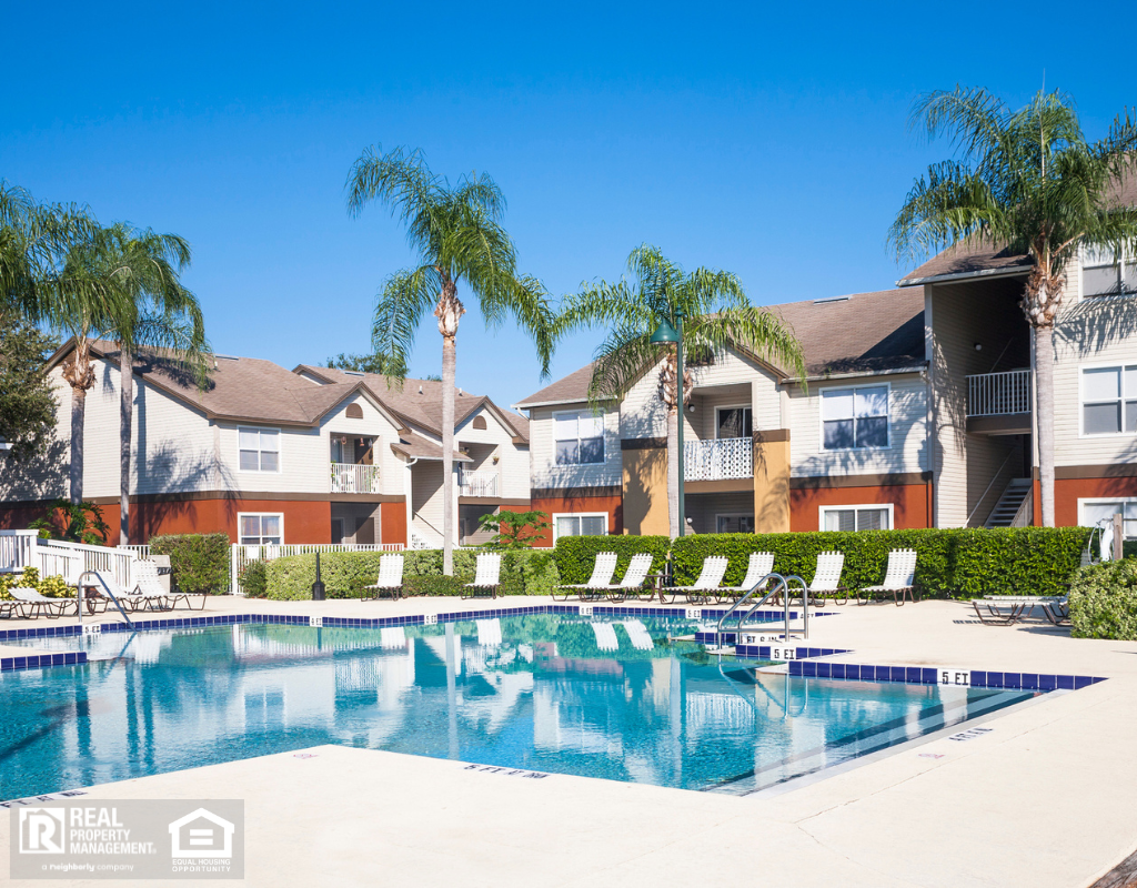 Swimming pool at a condominium complex. Palm trees, chaise lounge, clear sky.