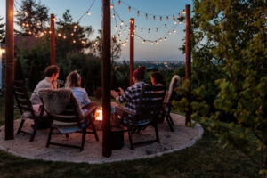 A group of four people sitting next to a burning fire pit at sunset. 