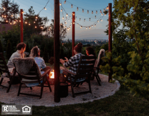 A group of four people sitting next to a burning fire pit at sunset.