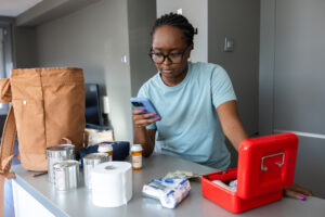 A woman evaluates medicine bottles and items on a countertop, preparing for emergencies. 