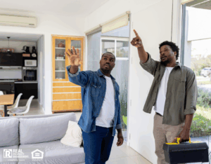 Two men discussing home repairs while pointing at an area in a living room.
