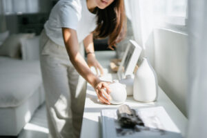 Young woman enjoys time at home, decorating and organizing picture frames and vases on the shelf by the window