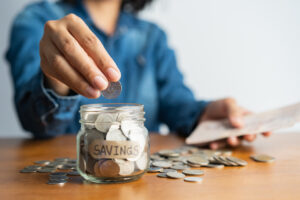 A person saving money by putting coins into a jar.