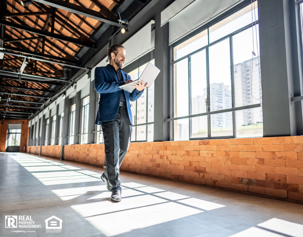 A man in a suit walks through a vacant building holding a laptop.
