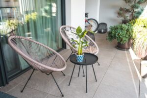 A stylish outdoor seating area with rattan chairs and a central table featuring a potted plant, set on a sleek tiled patio.