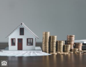 A small house model next to a pile of coins on a wooden table, symbolizing investment in real estate.