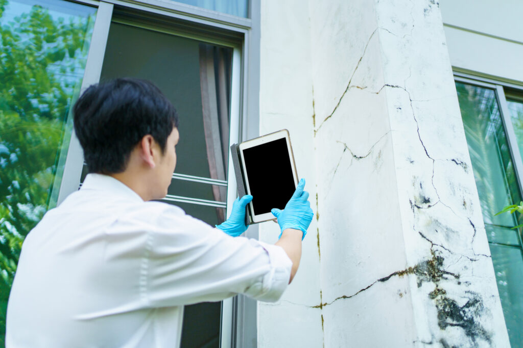A man in blue gloves takes photos of damaged home with a tablet, focused on crisis management.