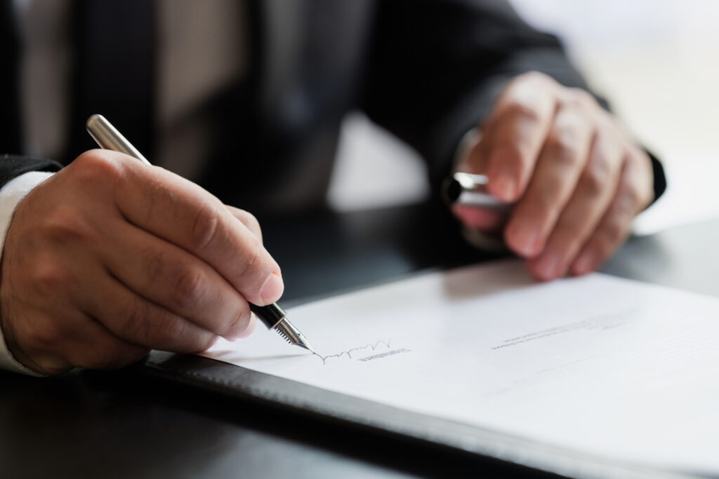 A person in a suit signing a document at a desk.