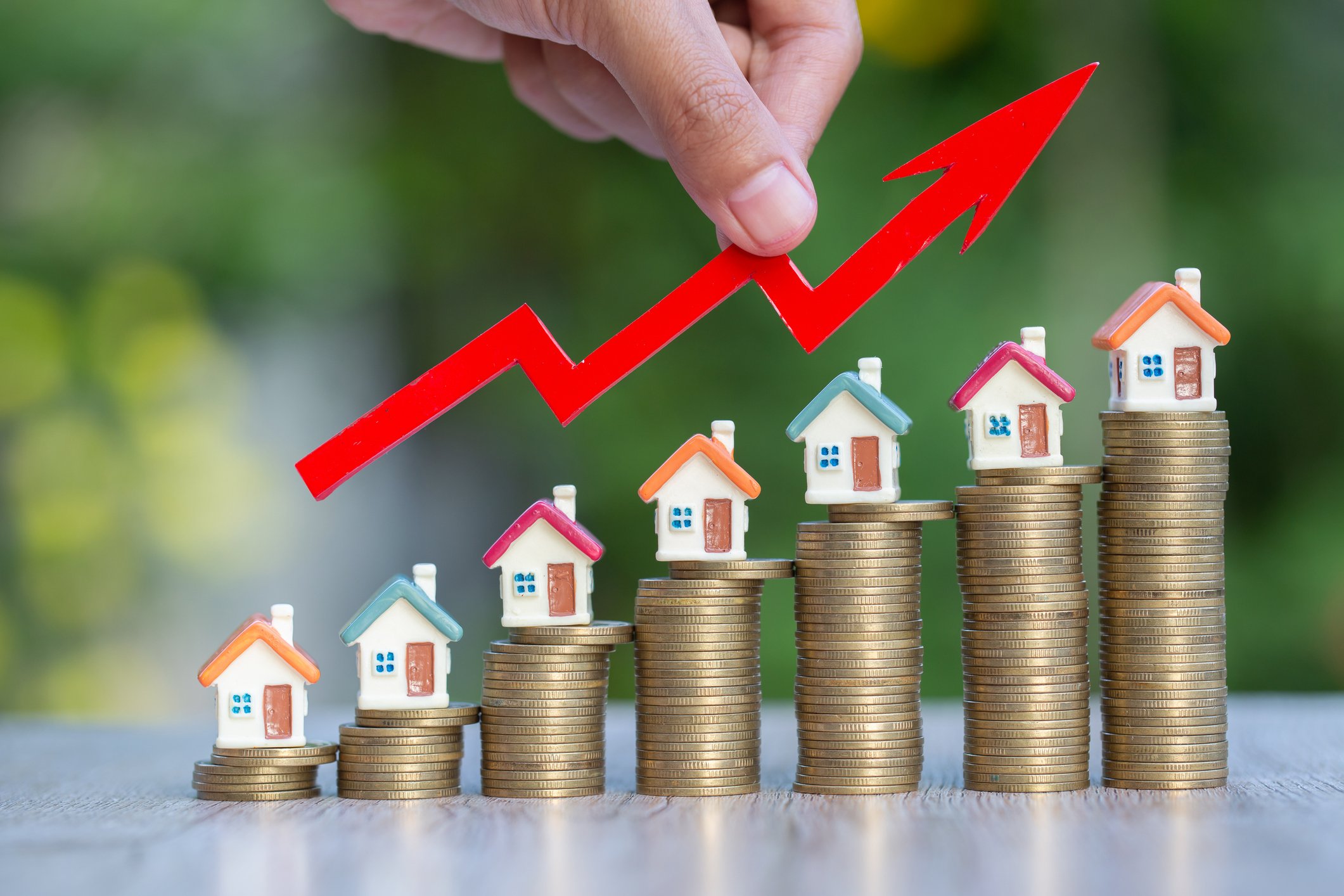 Tiny model homes placed upon stacks of coins from low to high, with a red arrow representing growth from initial investment.
