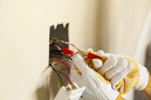 An electrician is replacing a wall switch. A DIY project concept. High voltage danger. The professional wearing shockproof gloves is tightening wire nuts