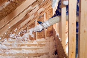 Spraying Blow-In Fiberglass Insulation Between the Attic Trusses of Your Alexandria Rental Home
