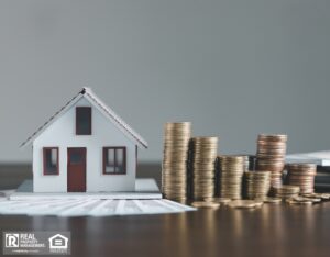 A small house model next to a pile of coins on a wooden table, symbolizing investment in real estate.