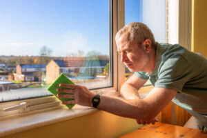 Man wiping condensation with a green sponge to prevent mold from forming.
