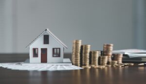 A small house model next to a pile of coins on a wooden table, symbolizing investment in real estate.
