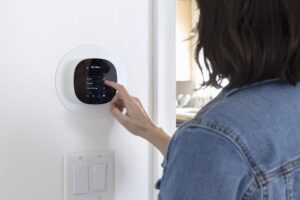 A woman programming a smart thermostat at home.