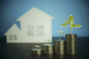 A house alongside small plants sprouting from stacks of coins, representing income generation
