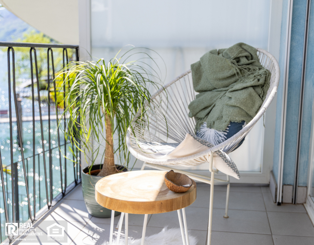 Cozy balcony featuring a modern chair with a green throw, a potted plant, and a small wooden table in bright sunlight.