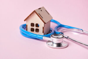 Medical stethoscope and toy house on a pink background with copy space