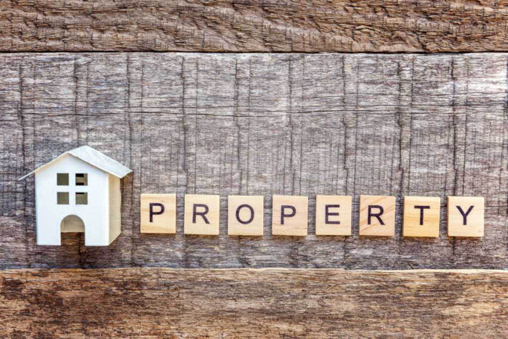 A small home next to wooden blocks spelling out “property,” real estate investment advice to get income property education.