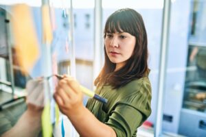 Property manager writing notes on a glass wall in an office, strategizing maintenance efforts.