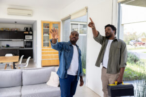 Two men discussing home repairs while pointing at an area in a living room.
