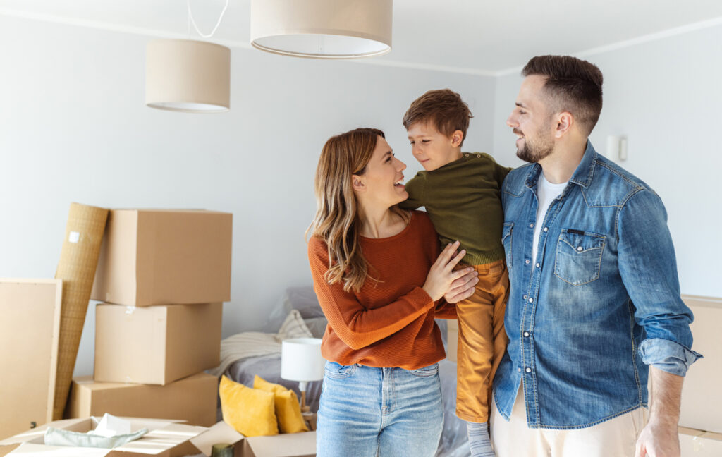 Shot of a happy family with one child standing in new living room surrounded by boxes