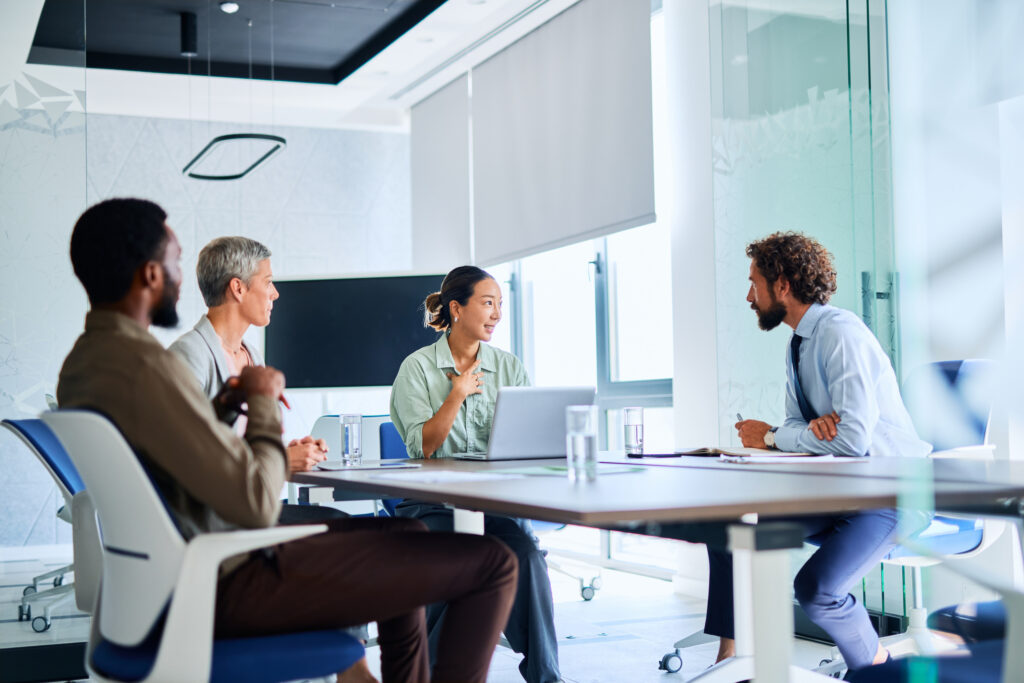 Four businesspeople sitting around a table in a modern office, engaging in a project discussion.