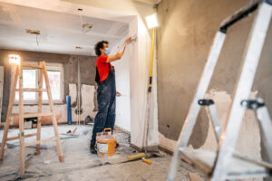 Construction worker plastering and smoothing concrete wall in room of flipped home.