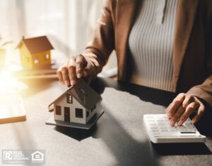 Woman sitting at a desk with model home and calculator.