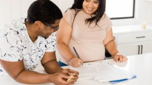 Smiling couple sitting at a kitchen table reviewing and signing lease papers, symbolizing teamwork and clear communication in property management.