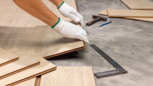 Worker installing luxury vinyl plank flooring on a concrete subfloor during a renovation project.