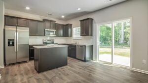 Modern kitchen with stainless steel appliances, dark cabinetry, and natural light from sliding glass doors.
