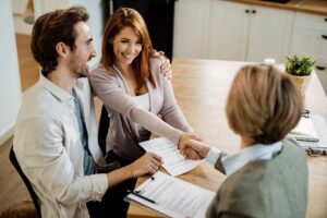 Young happy couple shaking hands with property manager while having a meeting.