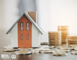 House model and money coin stacks on table, blurred background.